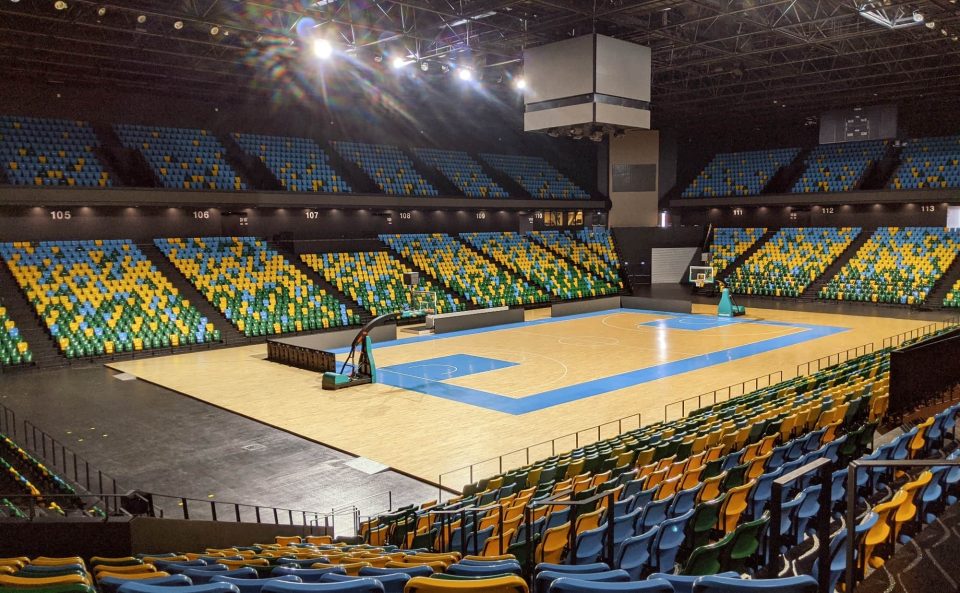An empty basketball arena is shown , looking down at the court from blue, yellow, and green stadium seating.