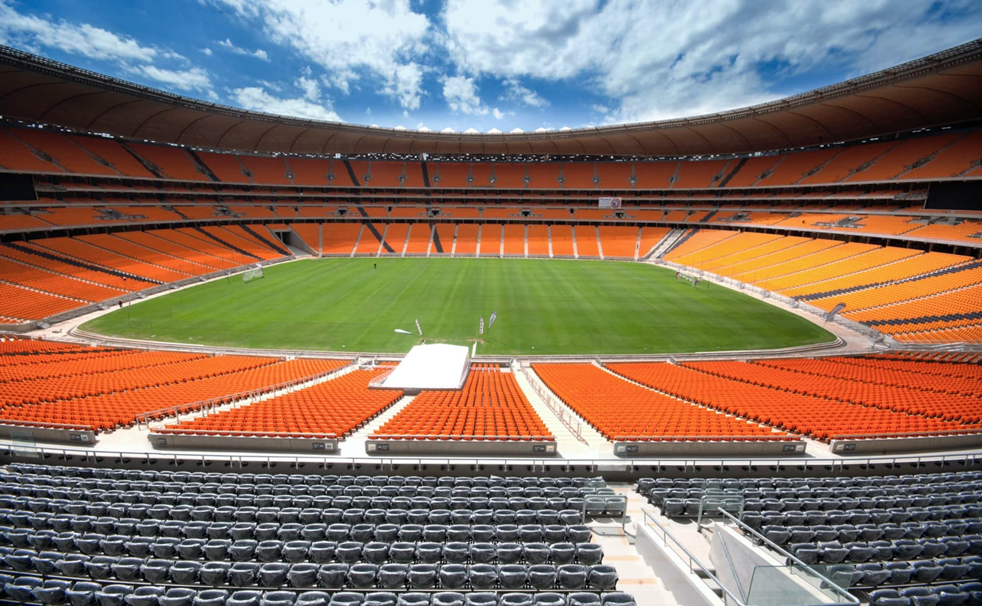 An empty sports stadium looking down at the green field from gray and orange seating.