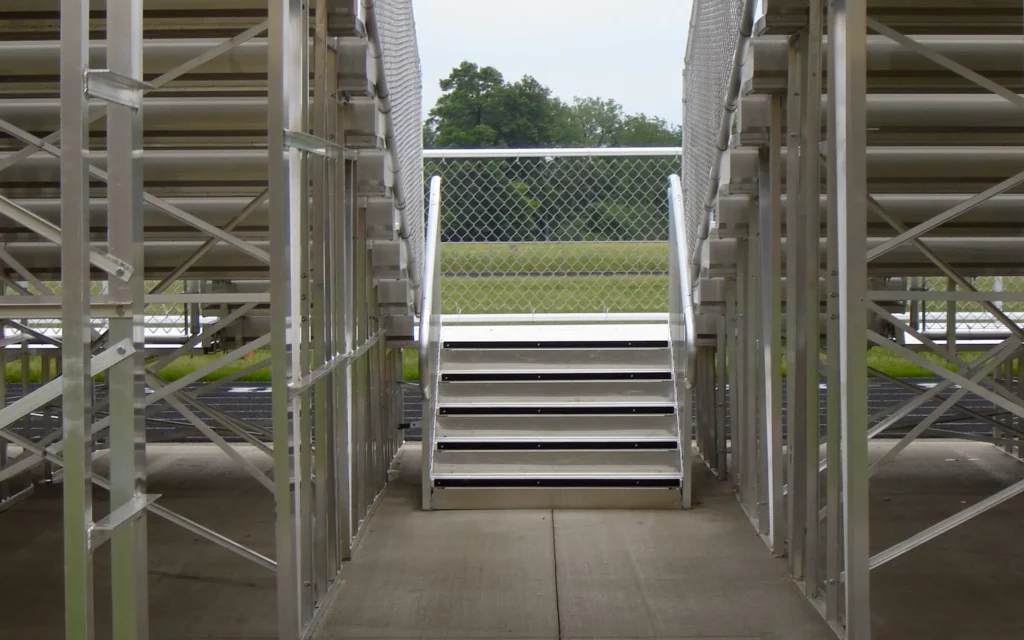 Underside view of outdoor elevated bleachers and stairs leading on to the the athletic field.
