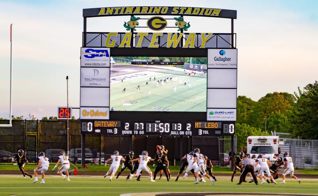 Outdoor football scoreboard and videoboard with two teams competing below.