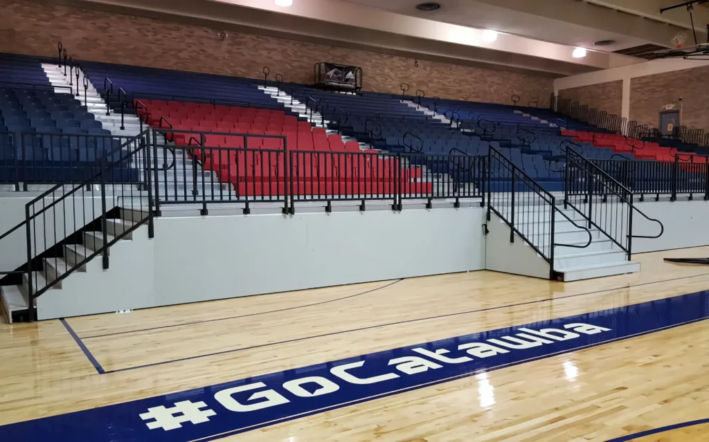 Red and blue indoor telescopic bleachers are expanded in a gym.