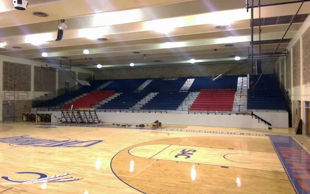 Blue and red indoor telescopic bleachers are expanded in a gym.