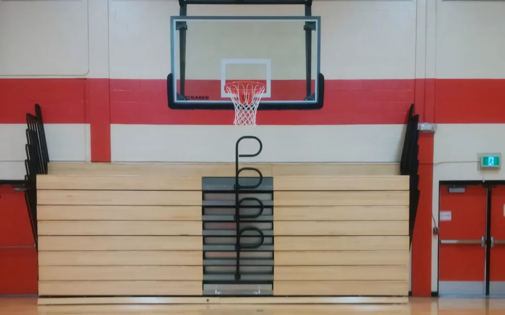 Wood-finished indoor telescopic bleachers are retracted and stored in a gym.