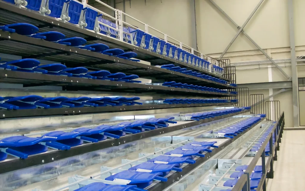 Blue indoor telescopic bleachers are a mix of expanded and retracted with all seats folded down for storage.
